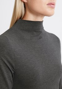 Pilkas aukštas kaklas sukurta iš minkštos, tamprios medžiagos. Praėjusio dizaino, su lygiu paviršiumi ir minimaliais siūlėmis. Artimas kaklo apipavidalinimo vaizdas.