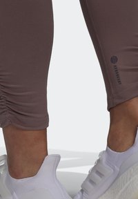 Brune, tætsiddende leggings med rynkede detaljer ved kanten. Kombineret med hvide træningssko med mesh-overdel og tekstureret sål.