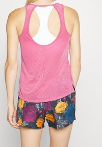 Růžový bezrukávový síťový top s kulatým vykrojením na zádech, doplněný květinovými šortkami s žlutými, fialovými a modrými růžemi.