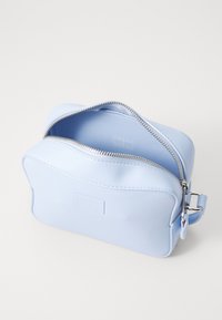 Světle modrá kosmetická taška vyrobená z hladkého materiálu, s uzavřením na zip, zaoblenými okraji a decentním logem na jedné straně.