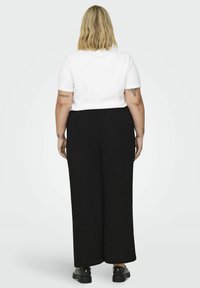 Camiseta de algodón blanca con mangas cortas, combinada con pantalones de pierna ancha negros de cintura alta, usados con zapatos negros de cordones.