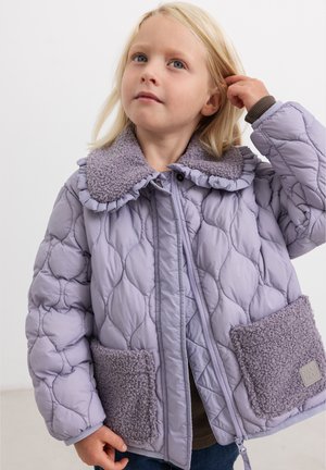 Jeune enfant aux cheveux blonds portant une veste matelassée violet clair avec un col texturé et de grandes poches avant, regardant légèrement vers le haut.