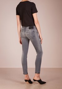 Jeans skinny grises con tiro bajo, bolsillos traseros y una ligera textura desgastada, combinados con una camiseta negra ajustada y mule de tacón negro.