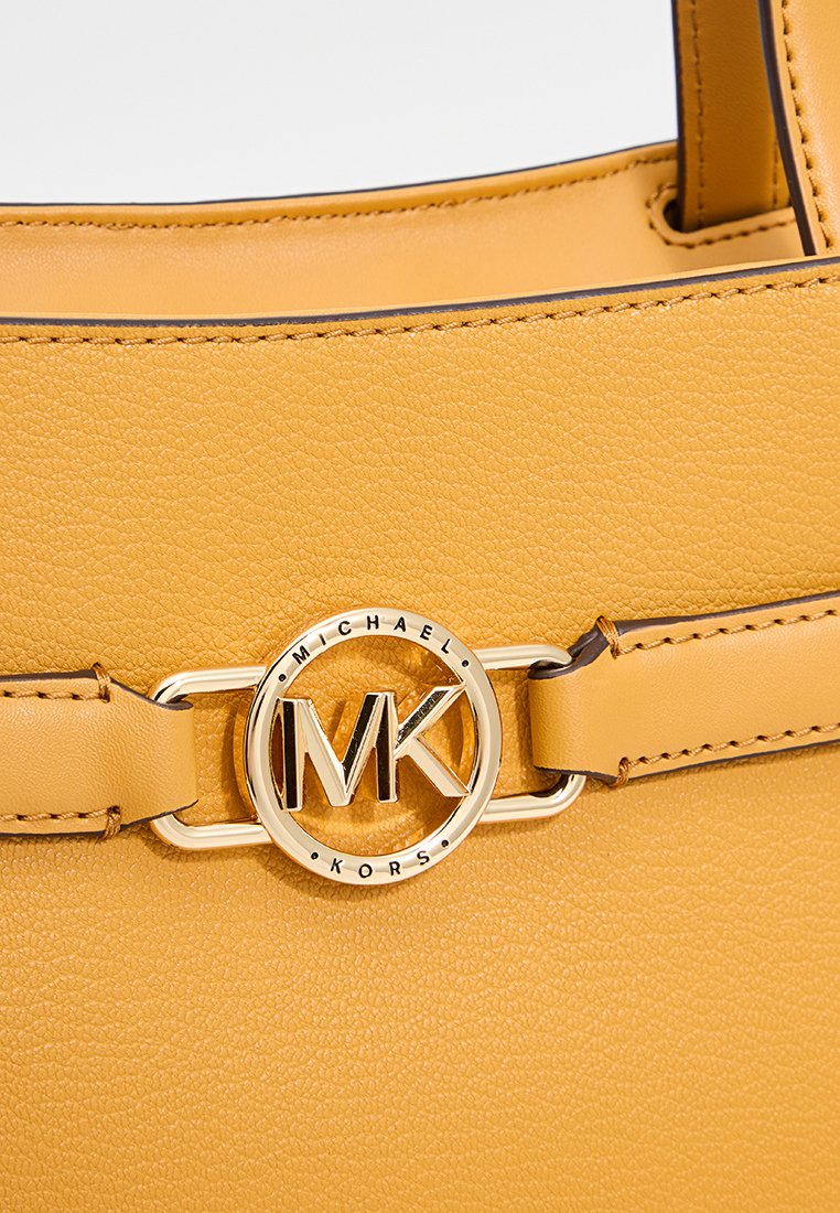 Sac à main en cuir jaune avec un fermoir rond en or portant les initiales "MK" et un design épuré. Accents cousus sur la poignée.