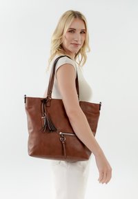 Borsa tote in pelle marrone con spallacci, tasca con cerniera e dettaglio di nappina. Texture morbida con finitura liscia e design spazioso.