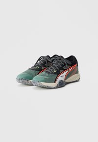 Scarpe sportive multicolore con tomaia in rete verde e nera, suola in gomma testurizzata e accenti bianchi e arancioni a contrasto.