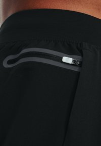 Pantaloncini sportivi neri con tasca con cerniera dotata di una linguetta bianca e tessuto liscio ed elastico. I dettagli delle cuciture sono visibili intorno alla vita.