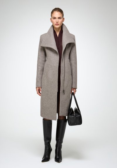 Cappotto di lana grigio con colletto alto, zip frontale, tasche laterali e vestibilità su misura, abbinato a stivali neri in pelle al ginocchio e a una borsa nera.