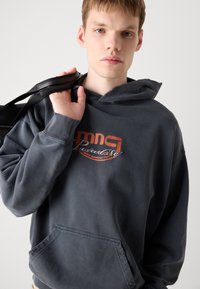 Sudadera gris oscuro con un bolsillo frontal, presenta un logo gráfico colorido. Tejido de mezcla de algodón con un cuello y dobladillos ligeramente desgastados.