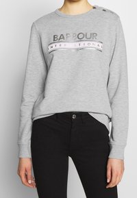 Light grey sweatshirt featuring "Barbour International" printed in metallic font, round neck, ribbed cuffs, and decorative shoulder buttons.
