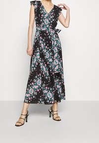 Blommig maxiklänning i svart tyg, med V-ringning, volangärmar, knyt i midjan och ett mönster av rosa och gröna blommor genom hela.