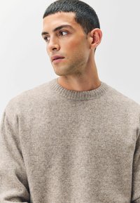 Jersey de cuello redondo beige hecho de una tela suave y texturizada, con un collar acanalado y un ajuste ligeramente holgado.
