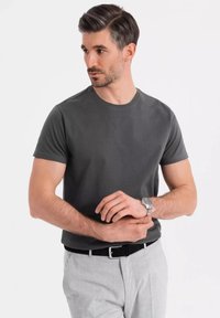Grå kortærmet t-shirt med rund hals, kombineret med lysegrå bukser og et sort bælte. Sølvur på håndleddet.