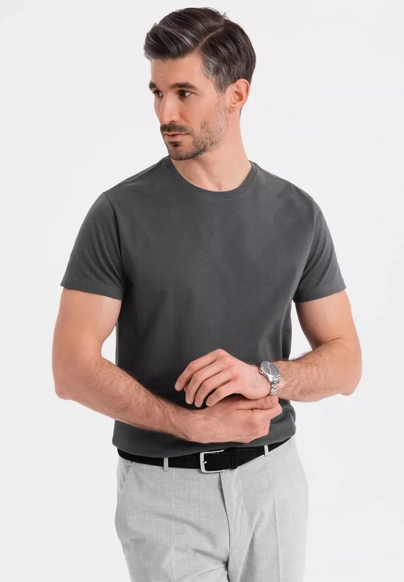 Grå kortærmet t-shirt med rund hals, kombineret med lysegrå bukser og et sort bælte. Sølvur på håndleddet.