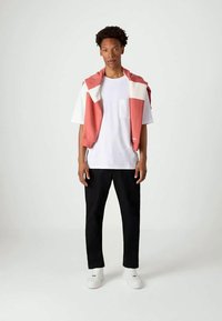 Tricou alb, pulover corai deschis drapat peste umeri, pantaloni negri și adidași albi. Design simplu, croială lejeră și culori solide.