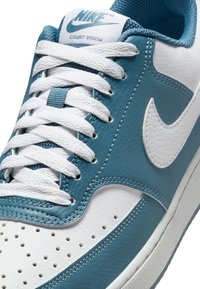 Sneaker Nike Court Vision con tomaia in pelle bianca e verde mare, lacci bianchi rotondi, punta perforata e logo swoosh bianco.