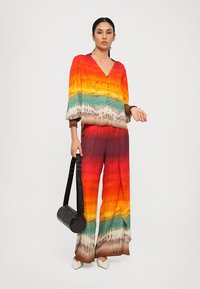 Bunter Look mit einem lässigen Oberteil mit V-Ausschnitt und weit geschnittenen Hosen. Der Stoff ist seidig, mit einem Farbverlauf von Orange zu Rot, Teal und Braun.