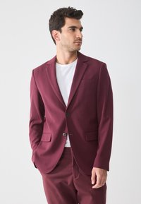 Blazer burdeos con solapas de pico, dos bolsillos frontales, cierre de un botón, textura de tela suave, combinado con una camiseta blanca.