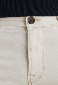 Jean en denim couleur crème avec une fermeture à bouton en métal et une couture légèrement contrastante. Présente une coupe droite et des poches latérales.