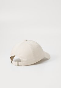 Beige cotton baseball cap with a curved visor, adjustable strap at the back, and stitched detailing on the crown. No visible logos.