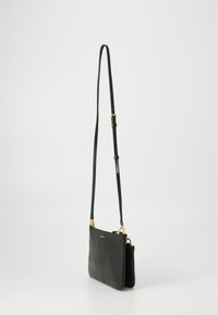 Borsa a tracolla nera in pelle con una texture liscia, hardware in tonalità oro, tracolla regolabile e un design minimalista caratterizzato da una chiusura con zip.