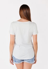 T-shirt blanche à manches courtes avec un col rond, texture douce et ourlet incurvé, associée à un short en denim bleu clair.