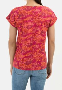 Top de manga corta en rosa y naranja con un patrón ondulado. Hecho de una tela ligera. Presenta un escote redondeado y un corte relajado.