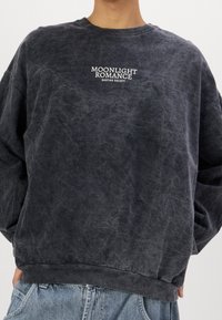 Tummanharmaa collegepaita, jossa on teksturoitu pinta, pyöreä kaula-aukko ja ylimitoitettu leikkaus. Edessä valkoisella graafisella tekstillä "MOONLIGHT ROMANCE".