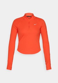 Narančasta sportska košulja dugih rukava s pola patent zatvaračem, izrađena od lagane, rastezljive tkanine. Sadrži Nike logo na prsima.