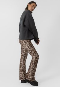 Felpa grigia oversize con un logo nero sulla schiena, abbinata a pantaloni a zampa d'elefante con stampa leopardata e stivali platform neri e massicci.