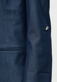 Μανίκι σκούρου μπλε σακακιού με ασημί μανικετόκουμπο και οριζόντια τσέπη με άνοιγμα στο πλάι.