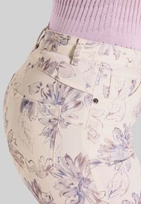 Blumenmuster-Hose in Creme mit lila Akzenten. Verfügt über Gesäßtaschen und ein körperbetontes Design. Hergestellt aus leichtem Stoff mit weicher Textur.
