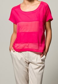 Fuksjowa bluzka z krótkim rękawem, z przezroczystym poziomym wzorem, okrągłym dekoltem i luźnym krojem, zestawiona z jasnymi spodniami w kant.
