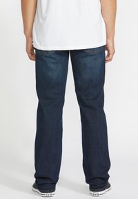 Jeans de mezclilla azul oscuro con un corte relajado, diseño de cinco bolsillos, un ligero desvanecimiento y detalles de costura en los bolsillos traseros.