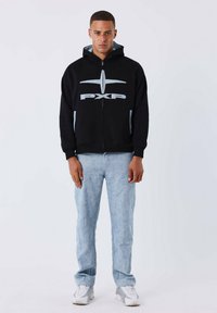 Sudadera con cremallera negra con acentos y logotipo en azul claro; combinada con pantalones de paisley azul claro y zapatillas blancas. Tela suave, corte relajado.