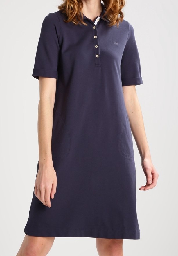 Femme portant une robe polo bleu marine à manches courtes avec des boutons sur la poitrine et un petit logo brodé sur le côté gauche.