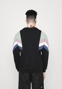 Sudadera negra con un diseño de bloques de color que presenta rayas verdes, rosas, blancas y azules en los hombros. Textura de tela suave.