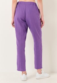 Paarse linnen broek met een relaxte pasvorm, elastische tailleband en zijzakken. De zoom eindigt boven de enkel en is gecombineerd met witte sneakers.