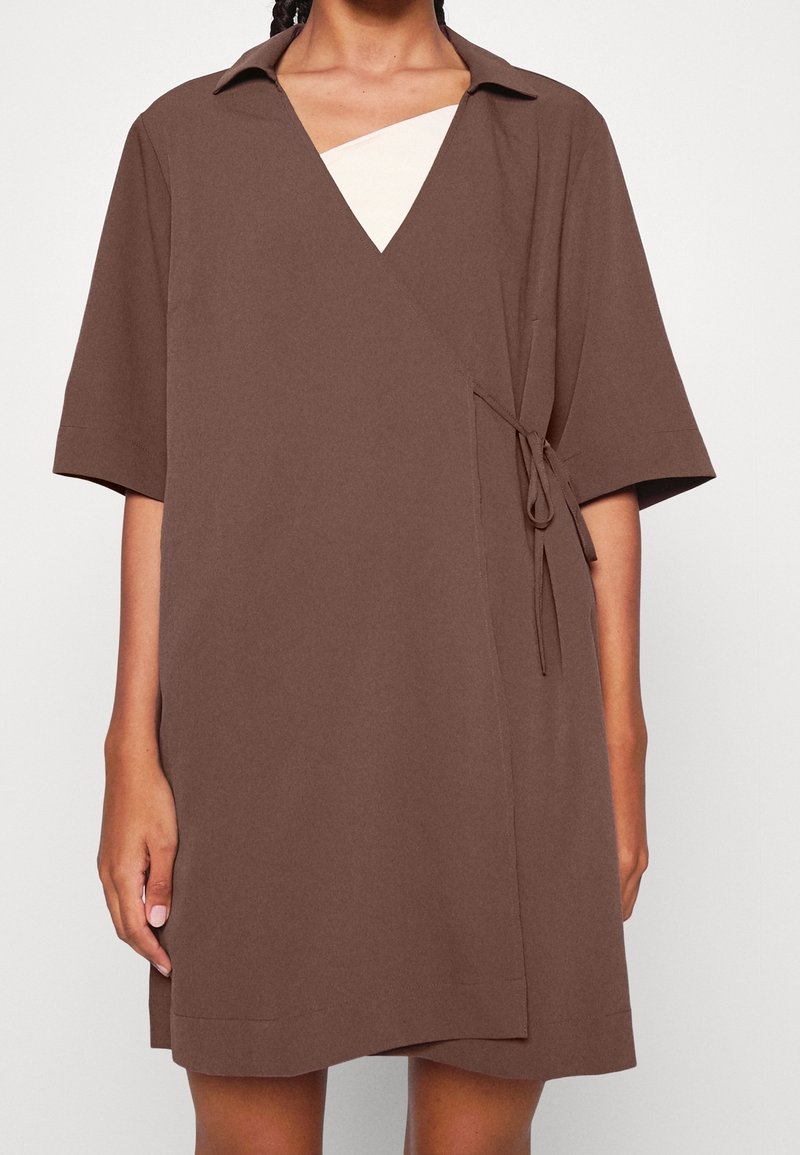 Robe portefeuille marron à manches courtes, col, encolure en V et détail noué à la taille. Tissu lisse avec un design simple et structuré.