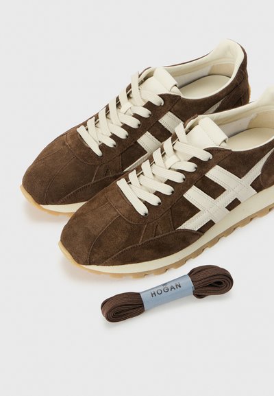 Braune Wildleder-Sneaker mit cremefarbenen Schnürsenkeln und seitlichen Akzenten, ausgestattet mit einer dicken cremefarbenen Mittelsohle und einer braunen Gummisohle. Enthält zusätzliche braune Schnürsenkel.