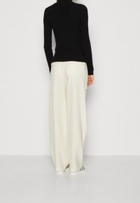 Maglione a collo alto nero a costine, pantaloni larghi crema a vestibilità ampia e sneaker bianche con strisce nere. Outfit semplice e moderno.