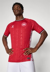 Rode voetbalshirt met korte mouwen, voorzien van textuurpatronen, zwarte accenten en een ronde halslijn. Bevat een logo op de borst en details aan de zijkanten.