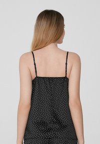 Camisón de satén negro con tirantes finos ajustables, que presenta un respaldo fruncido y lunares blancos en toda la tela.