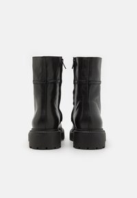 Botines negros de cuero con acabado liso, que cuentan con una cremallera trasera y una suela negra gruesa con un patrón de tracción texturizado.