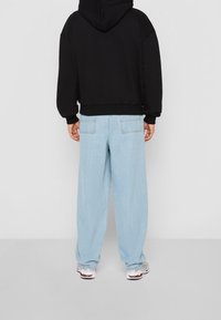 Černá mikina s kapucí v uvolněném střihu, doplněná světle modrými širokými džínami. Jednoduchý design bez viditelných vzorů či akcentů.
