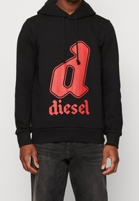 Svart huvtröja med en framträdande röd "d"-logotyp och texten "diesel". Har en dragsko till huvan och ett mjukt, texturerat tyg.