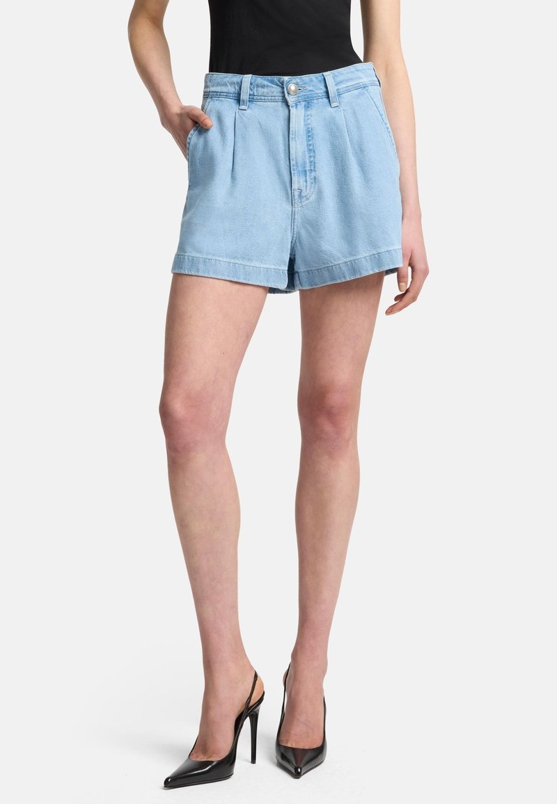 Shorts in denim blu chiaro con vita alta, caratterizzati da pieghe frontali e tasche laterali, abbinati a tacchi alti neri a punta.
