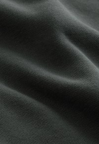 Tmavosivá tkanina s jemnou rebrovanou textúrou a jemnými záhybmi vytvárajúcimi mäkké tiene a zvýraznenia.