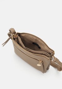 Beige schoudertas met twee ritssluitingen, gouden metalen details en een stoffen voering. Voorzien van een verstelbare schouderband en een kleine logotag.