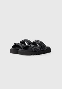 Black open-toe sandals with thick textured soles and two adjustable straps featuring buckles and decorative stitching.